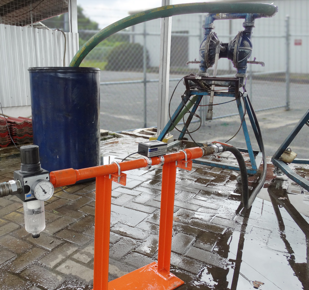 Pneumatic diaphragm transfer pump with connected hoses beside an industrial container